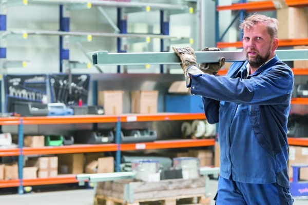 Ein Mann trägt ein langes Metallstück auf seiner Schulter durch eine Werkshalle Ein Mann trägt ein langes Metallstück auf seiner Schulter durch eine Werkshalle