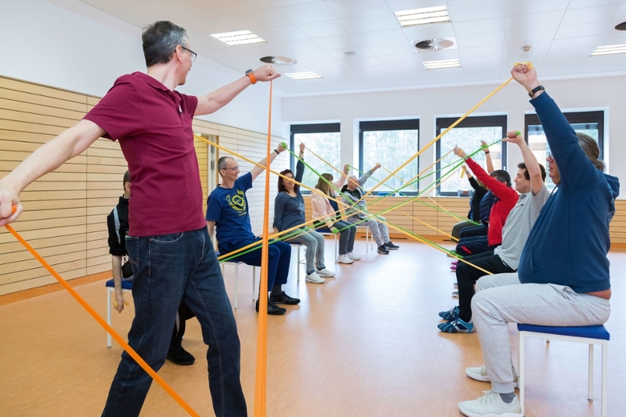 Mehrere Personen machen gymnastische Übungen mit farbigen sogenannten Thera-Bändern. Mehrere Personen machen gymnastische Übungen mit farbigen sogenannten Thera-Bändern.