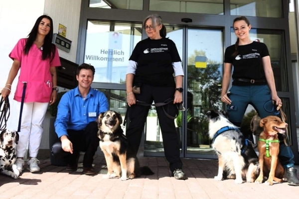 Mitarbeiter der Klinik und des Tierheim mit Hunden vor dem Eingang der Rheumaklinik