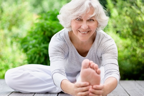 Eine Frau mit grauen Haaren macht Entspannungsübungen im Grünen und schaut dabei in die Kamera. Eine Frau mit grauen Haaren macht Entspannungsübungen im Grünen und schaut dabei in die Kamera.
