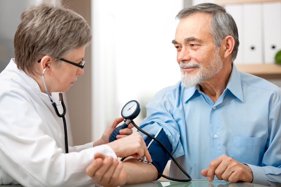 Eine Ärztin misst bei einem Patienten mit grauem Haar mit einem Gerät den Blutdruck.